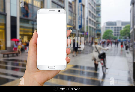 Das Smartphone in der Hand der Frau mit isolierten weißes Display für Mock-up. Straße im Hintergrund. Stockfoto