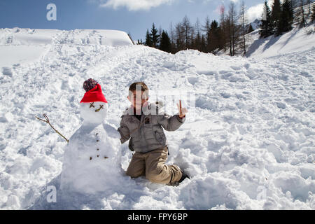 Kind mit Schneemann mit orange Wolle Hut und blauer Himmel Stockfoto