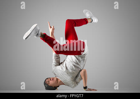 Eine jungen Mann im lässigen roten Jeans Ausarbeitung passen, auf dem Boden bewegt sich Breakdance durchführen. Voller Länge Foto Studio grau ba Stockfoto