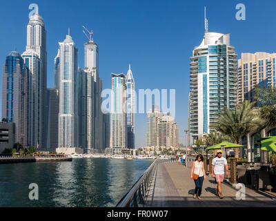 Menschen zu Fuß auf der Promenade, Boote und Highrise Waterfront-Gebäude im Stadtteil Marina von Dubai, Vereinigte Arabische Emirate Stockfoto