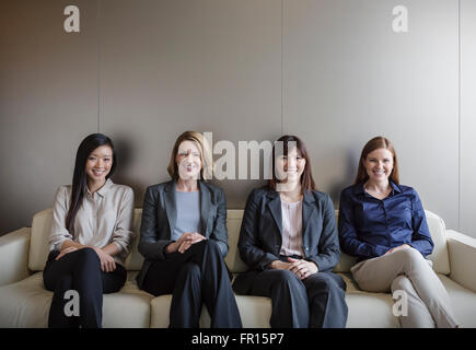 Porträt, Lächeln Geschäftsfrauen sitzen in einer Reihe auf sofa Stockfoto