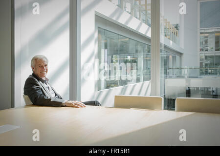 Porträt lächelnd senior Geschäftsmann im sonnigen Konferenzraum Stockfoto