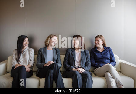 Lächelnde Unternehmerinnen sprechen in einer Reihe auf sofa Stockfoto