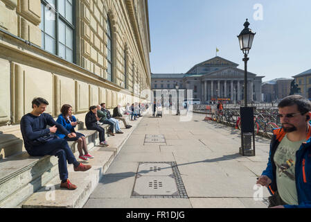 Leute sitzen an der königlichen Königsbau Palast und Theater in München genießen die warme Sonne im Frühling, Bayern, Deutschland Stockfoto