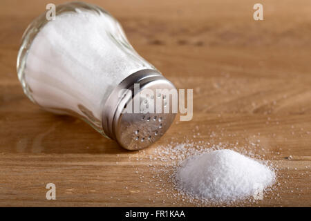 Traditionelle Glas Salzstreuer und verschüttetes Salz auf Holz Hintergrund Stockfoto