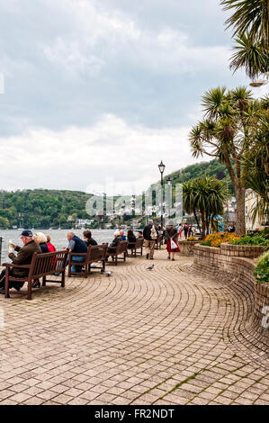 Braune Bänke locken Touristen zum entspannen und genießen die Aussicht, als Wanderer gemütlich vorbei an der malerischen roten Backstein-promenade Stockfoto