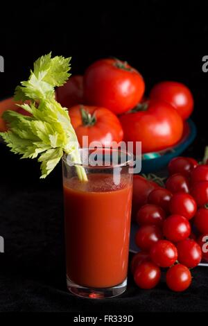 Bloody Mary cocktail mit einem Stiel von Sellerie und umgeben von frischen Tomaten in verschiedenen Größen auf einem schwarzen Hintergrund Stockfoto