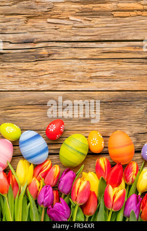 Bunte Ostereier und Tulpen auf hölzernen Hintergrund platziert Stockfoto