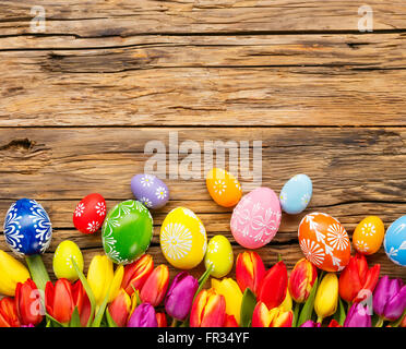 Bunte Ostereier und Tulpen auf hölzernen Hintergrund platziert Stockfoto