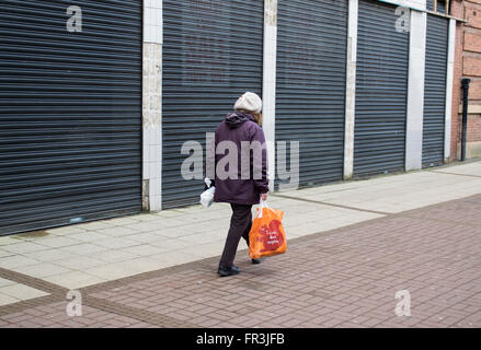 Eine Frau vorbei gehen eine Reihe von geschlossen Geschäfte im Stretford, Manchester, England, Großbritannien Stockfoto