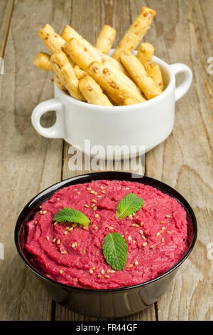 Rüben Hummus auf eine schwarze Schale und Brot-Sticks auf einer weißen Schüssel auf einem Holztisch Stockfoto