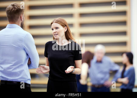 Geschäftsfrau, gestikulieren und im Gespräch mit Geschäftsmann in lobby Stockfoto