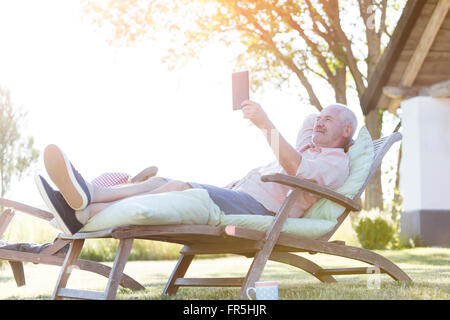 Senior woman mit digital-Tablette entspannend auf Liegestuhl im Garten Stockfoto