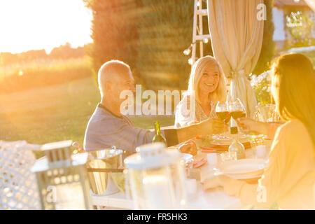 Senior paar eine erwachsene Tochter, die Weingläser an sonnigen Patio Tisch Toasten Stockfoto