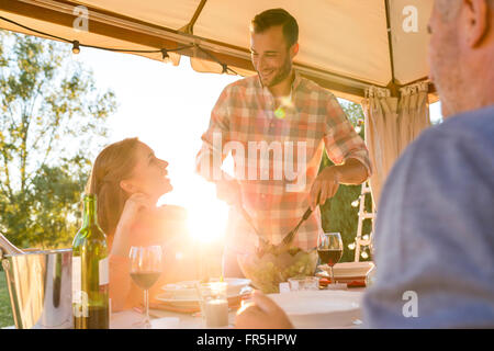 Junger Mann Portion Salat Frau an sonnigen Patio Tisch Stockfoto