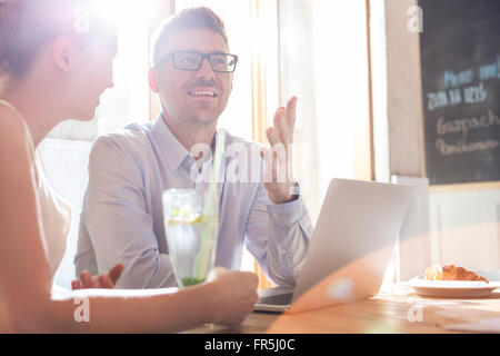 Geschäftsleute mit Laptop im sonnigen Café im Gespräch Stockfoto