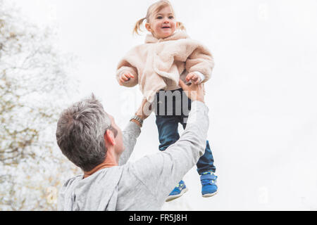 Vater anhebende Kleinkind Tochter overhead Stockfoto