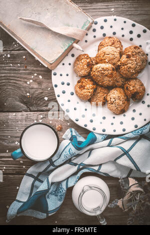 Buch, Haferflocken Cookies und eine Tasse Milch auf alten Boards vertikale Stockfoto