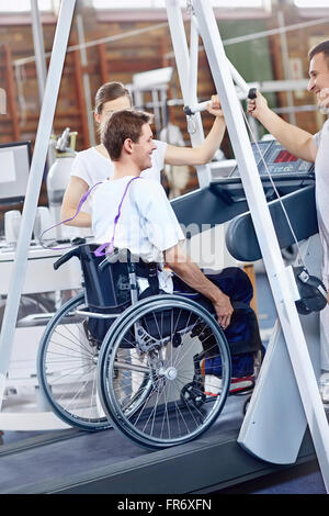 Physiotherapeuten führen Mann im Rollstuhl auf Laufband Stockfoto