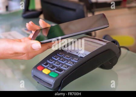 Frau mit NFC-Technologie am Markt, Shop, Kosmetikerin, Handy zu bezahlen. Kontaktloses bezahlen Stockfoto