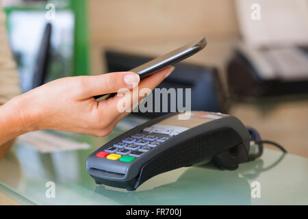 Frau mit NFC-Technologie am Markt, Shop, Kosmetikerin, Handy zu bezahlen. Kontaktloses bezahlen Stockfoto