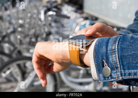 Frau in der Stadt mit Anwendung auf Smartwatch. Zeile der Fahrräder zu vermieten, Hintergrund Stockfoto