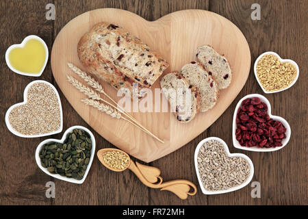 Cranberry Seed Brot Laib auf ein Holzbrett mit Weizen scheiden, Lovespoon mit Getreide, Kürbis und Sonnenblumen Samen in Herzform. Stockfoto