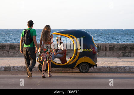 Das tägliche Leben in Kuba - Junges Paar Kreuzung Straße lokaler Mann in cocotaxi zu nähern, coco Taxi, bei El Malecon, Havanna, Kuba, Karibik, Karibik Stockfoto