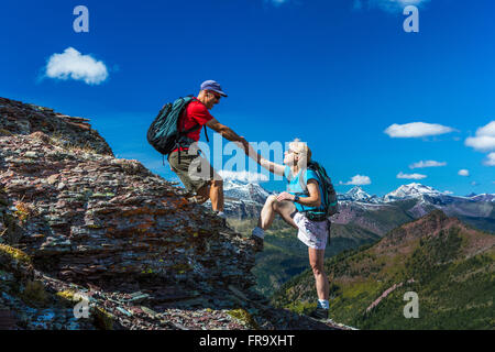 Männliche Wanderer helfen weibliche Wanderer auf einer Felsenspitze von einem Gebirgskamm grand Vista und blauer Himmel mit Wolken im Hintergrund Stockfoto