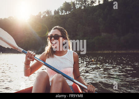 Lächelnde junge Frau auf einem See paddeln. Glückliche junge Frau an einem Sommertag in einem See paddeln. Stockfoto