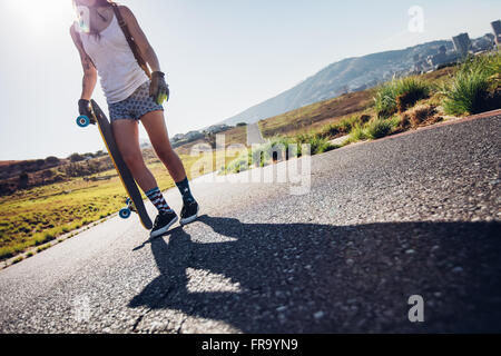 Aufnahme der jungen Frau zu Fuß mit ihrem Skateboard unterwegs beschnitten. Junge Frau mit einem Longboard an einem sonnigen Tag. Stockfoto