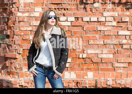 Ziemlich europäischen Mädchen mit Sonnenbrille mit Fotokamera gegen roten Backsteinmauer. Glückliche junge Frau am sonnigen Tag Stockfoto