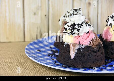 Neapolitanische Eis in Brownie Schüssel mit geschlagener Sahne und Schokolade Streusel. Stockfoto