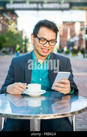 Erfolgreiche junge asiatische Mann in casual Geschäftskleidung lächelnd in entspannten outdoor-Café mit Tasse Kaffee mit Blick auf Stockfoto