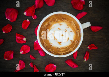 Eine Tasse Kaffee mit Latte Art und Blütenblätter stieg auf hölzernen Hintergrund Stockfoto