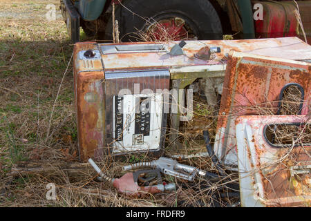 Verlassene antike Kraftstoffpumpe wird am Boden neben Lkw im Feld mit Unkraut überwuchert. Stockfoto