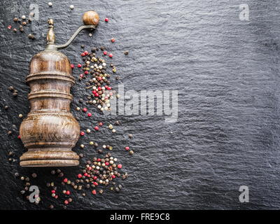 Bunte Pfefferkörner und alte Pfeffermühle auf dem schwarzen Hintergrund. Stockfoto