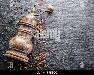 Bunte Pfefferkörner und alte Pfeffermühle auf dem schwarzen Hintergrund. Stockfoto