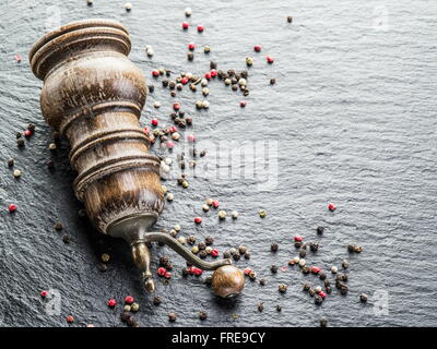 Bunte Pfefferkörner und alte Pfeffermühle auf dem schwarzen Hintergrund. Stockfoto