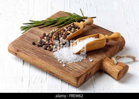 Salz, Pfeffer in hölzernen Schaufeln und Rosmarinus auf Holzbrett Stockfoto
