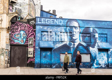 Zwei im mittleren Alter Männer zu Fuß vorne ein Stück der Straße Graffiti, die Förderung der Freisetzung von dem Krays Legende. Stockfoto