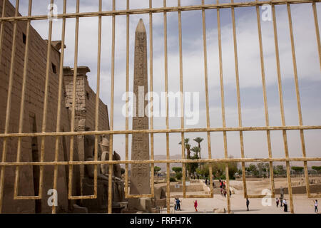 Durch Rost, Geländer, Touristen und der hohen Obelisk am Eingang des alten ägyptischen Luxor-Tempel, Luxor, Nil Senke, Ägypten gesehen. Der Tempel wurde gebaut von Amenophis III, von Tutanchamun abgeschlossen dann ergänzt durch Ramses II. Nach hinten ist ein Granit-Schrein, Alexander der große gewidmet und in einem anderen Teil war eine römische Feldlager. Der Tempel wurde fast Dauereinsatz als ein Ort der Anbetung bis in die Gegenwart. Stockfoto