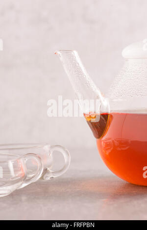 Schwarzer Tee im Glas Teekanne. Zwei Tassen aus Glas befinden sich auf der Seite auf einem Stein Küchentisch. Stockfoto