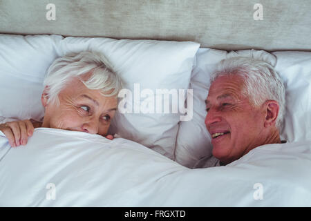 Gerne älteres paar sahen einander liegend auf Bett Stockfoto