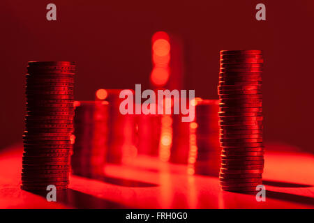 flache seitlicher Blick auf nebeneinander gestapelten Münzen im roten Licht bei Blende F5, 6; Die erste Zeile im Fokus Stockfoto
