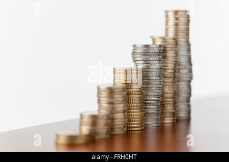 flache seitlicher Blick auf aufsteigende gestapelten Münzen nebeneinander auf eine glatte Holzoberfläche vor weiß Stockfoto