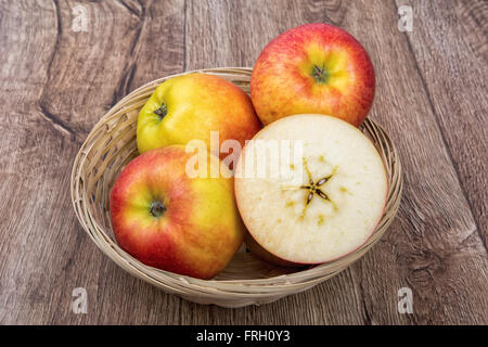 Äpfel in eine gestrickte Schale auf einem braunen Holz Hintergrund Stockfoto