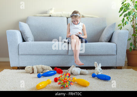 Es ist Zeit, um Ihre Spielzeuge zu bereinigen! Kleine Mädchen spielen mit Tablet-pc, wollen nicht die Reinigung zu tun. Stockfoto