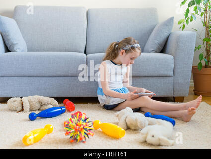 Es ist Zeit, um Ihre Spielzeuge zu bereinigen! Kleine Mädchen spielen mit Tablet-pc, wollen nicht die Reinigung zu tun. Stockfoto