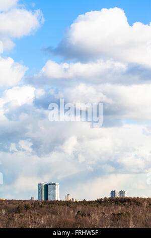 weißen Cumulus-Wolken am blauen Himmel über Wohnhäuser und Wäldern in sonniger Frühlingstag Stockfoto